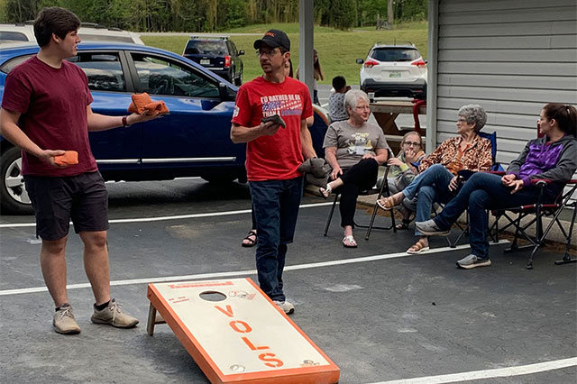 Cody and Thomas playing cornhole. Leta, Kaylee, Sheila, and Cara talking.